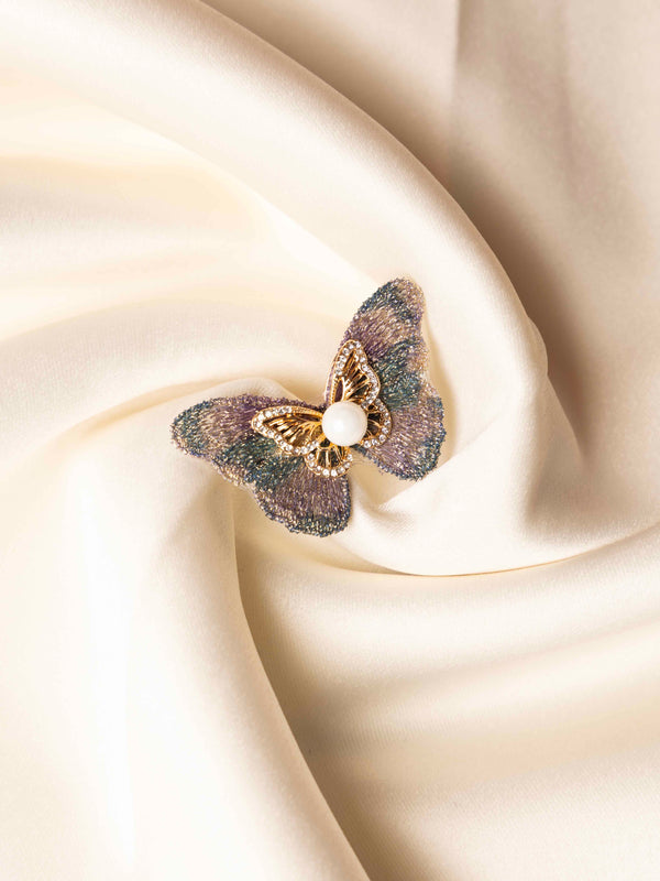 Butterfly-shaped brooch with pearl on a beige fabric background